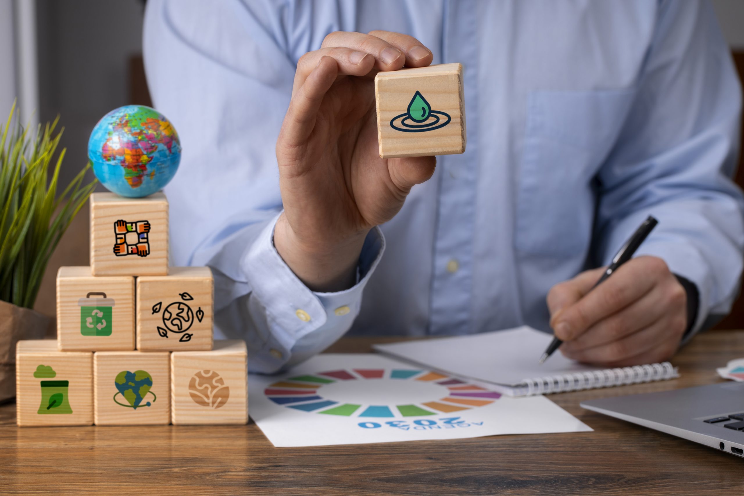 Mann sitzt am Schreibtisch und verfasst anhand hölzerner Blöcke mit Umwelt-Icons seine Nachhaltigkeitsagenda