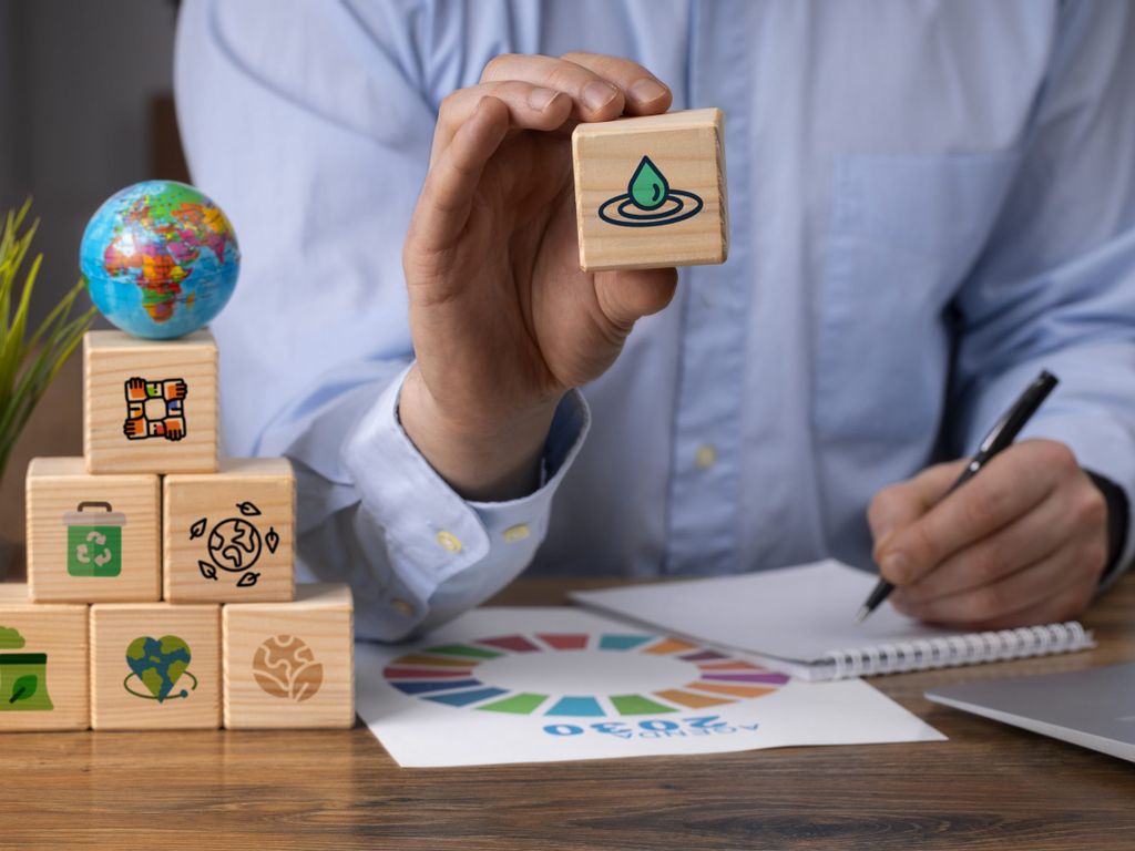 Mann sitzt am Schreibtisch und verfasst anhand hölzerner Blöcke mit Umwelt-Icons seine Nachhaltigkeitsagenda