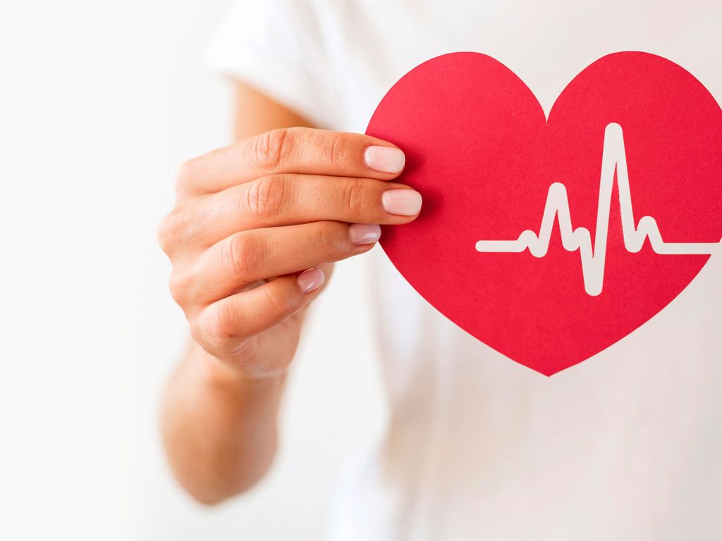 Frau hält Papierherz mit ausgeschnittenen Herztönen in die Kamera - Reminder an Gesundheitsmaßnahmen im Rahmen sozialer Nachhaltigkeit