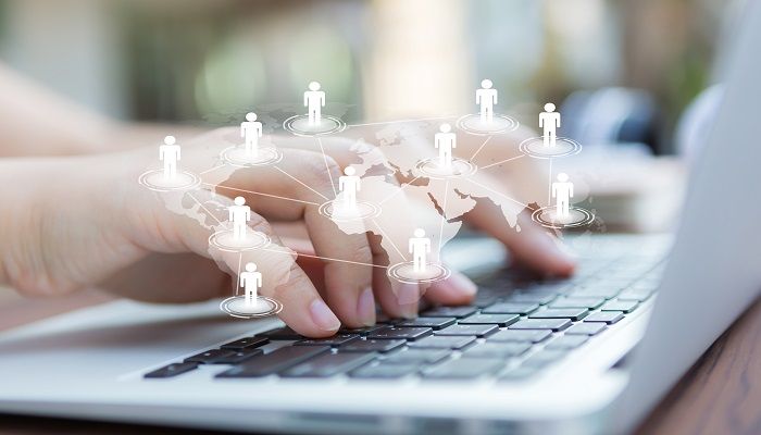 Hände beim Tippen, umgeben von einem Schatten der Weltkarte und Schatten von Menschen