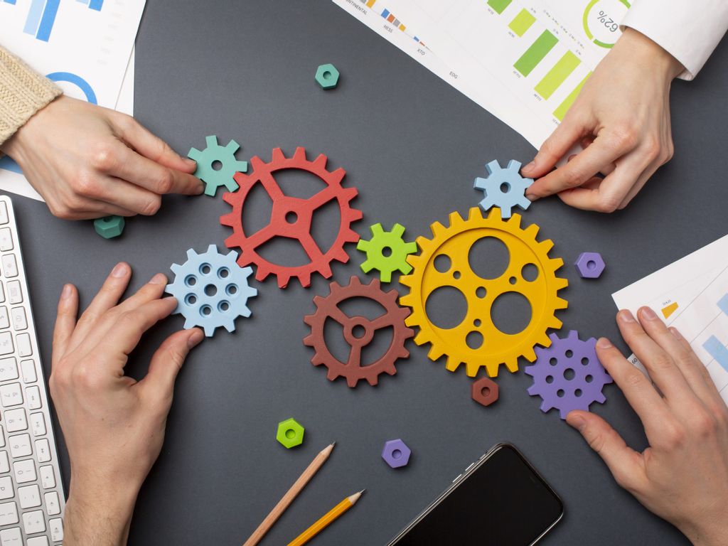 mehrere Geschäftleute sitzen an Tisch und arbeiten an nachhaltigen Entwicklungsprozessen symbolisiert durch verschiedene, bunte Zahnräder