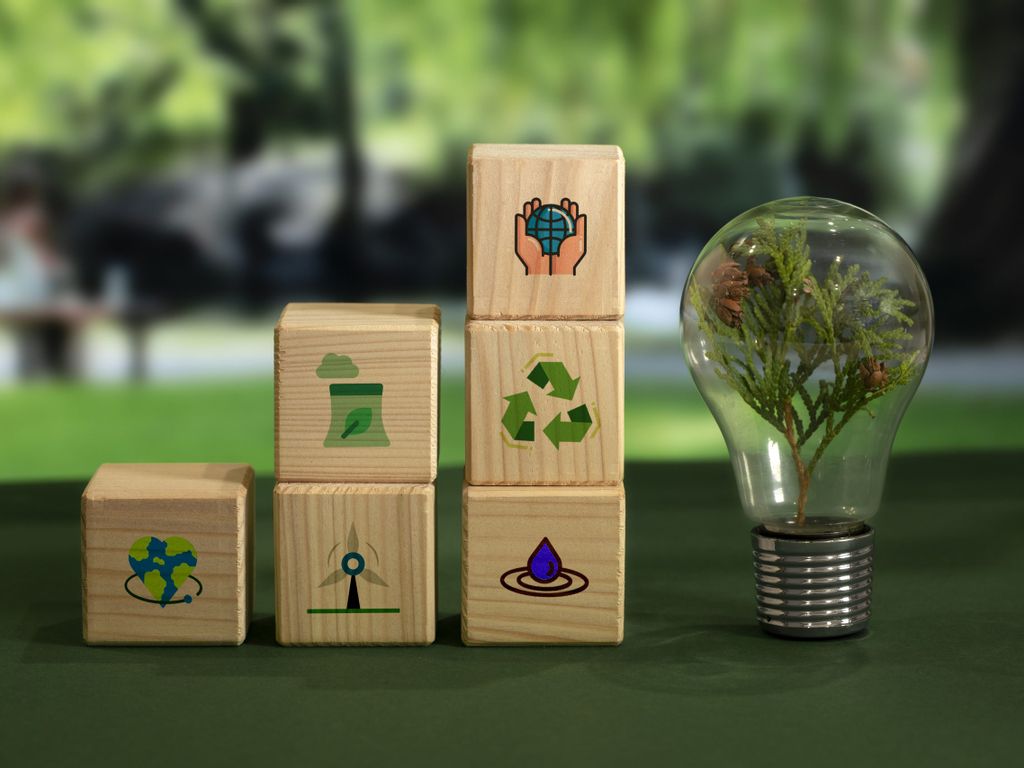 3 Stapel mit Holzblöcken mit verschiedenen Umwelticons und Glühbirne mit Zweig darin symbolisieren Notwendigkeit für Nachhaltigkeitsziele innerhalb der Unternehmensziele