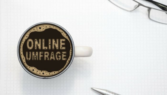 In einem Kaffebecher ist mit Kaffeeschaum Anschreiben Kundenbefragung geschrieben.