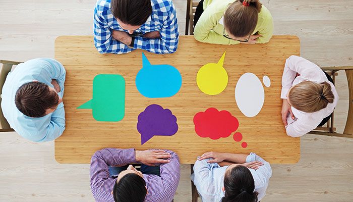 Sechs Menschen sitzen an einem Tisch und diskutieren über die Bedeutung von Mitarbeiterbefragungen.