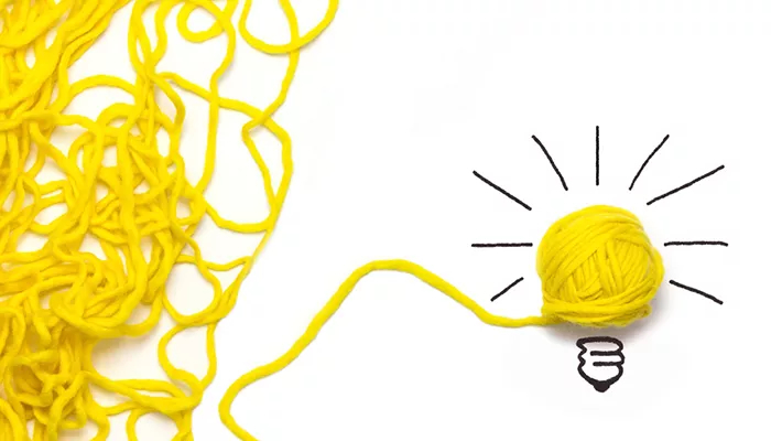 Gelbe Wolle liegt an der linken Seite und in der Mitte ist sie zu eine Wollknollen gerollt. Diese Knolle symbolisiert eine Glühbirne und ist von Zeichnungen ergänzt. Das Bild steht für einen Durchbruch beim Change Management.