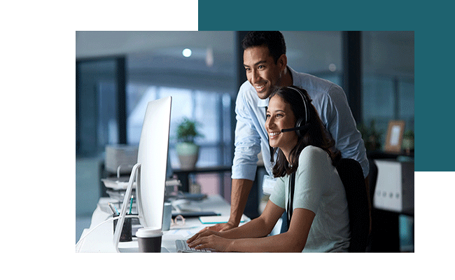 Eine Frau sitzt mit einem Headset am Computer und ihr Kollege unterstützt sie bei einer Community-Software.