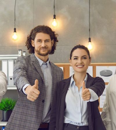 Mitarbeitende schauen lächelnd in die Kamera und zeigen mit dem Daumen nach oben. Ein Zeichen für einen hohen ENPS Wert.