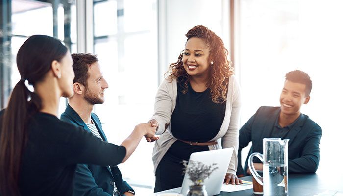 Eine Employee Experience Managerin trifft sich im Büro mit ihren Kollegen und reicht ihnen zur Begrüßung die Hand.
