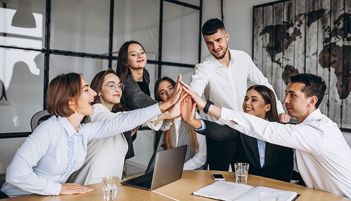 Ein junges Team sitzt zusammen und klatscht sich in der Mitte ab, weil sie eine gute Employer Branding im Unternehmen haben.