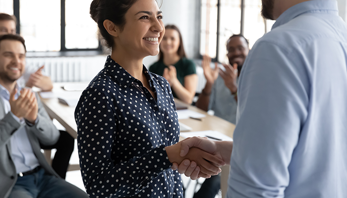 Zwei Kollegen schütteln sich im Büro die Hände und symbolisieren damit, dass ein detaillierter Feedbackprozess wichtig für Führungskompetenz ist.