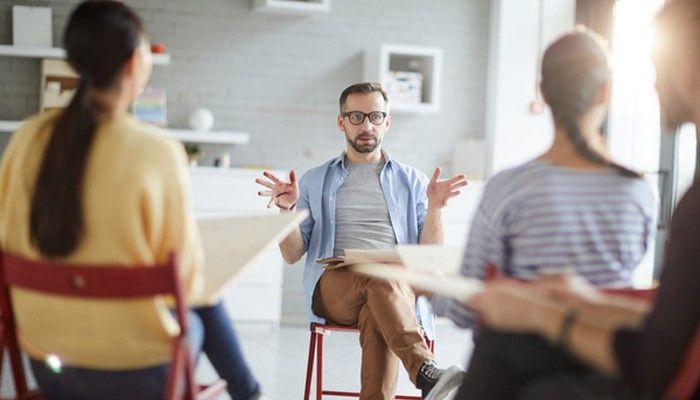 Ein Mann sitzt vor einer Gruppe und gibt ein Führungskräfte Coaching.