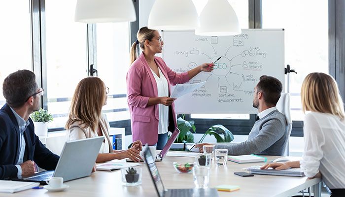 Eine Businessfrau hält vor ihren Kollegen eine Präsentation über SEO und Führungskräfte Coaching.
