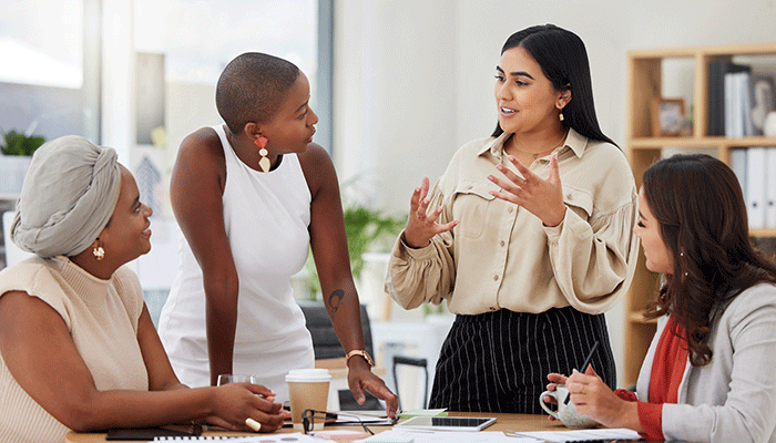 Vier Frauen stehen an einen Tisch und reden über das Führungskräfte Coaching.