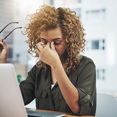 Eine Frau hat Kopfschmerzen und hält sich den Kopf. Ihr Arbeitgeber sollte eine Gefährdungsbeurteilung durchführen.
