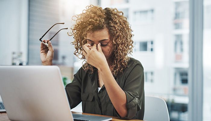 Eine Frau hat Kopfschmerzen und hält sich den Kopf. Ihr Arbeitgeber sollte eine Gefährdungsbeurteilung durchführen.
