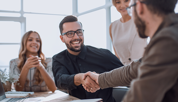Zwei Männer geben sich zufrieden am Tisch im Büro die Hand und feiern eine erfolgreiche Kundenbindung.