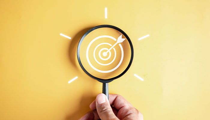 Durch Kundenpanel Zielgruppenfeedback einholen: Ein Mensch hält eine Lupe in der Hand, in deren Mitte sich eine Zielscheiben-Skizze befindet.