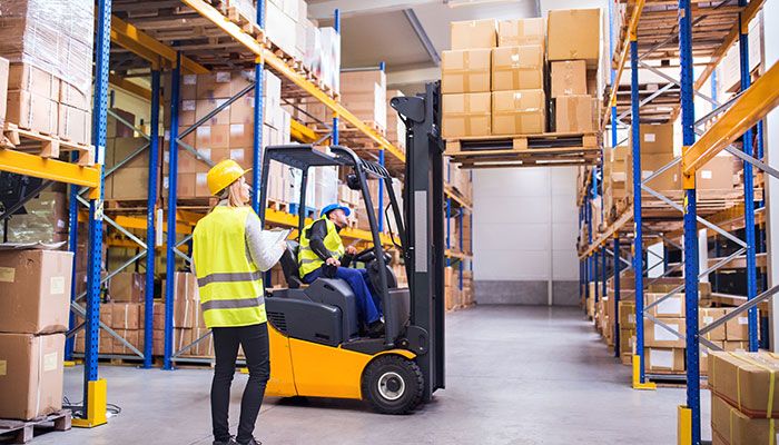 Eine Frau navigiert einen Mann auf einem Gabelstapler. Beide Mitarbeiter sind bei einem Mitarbeiterfeedback in der Industrie eingeschränkt erreichbar.