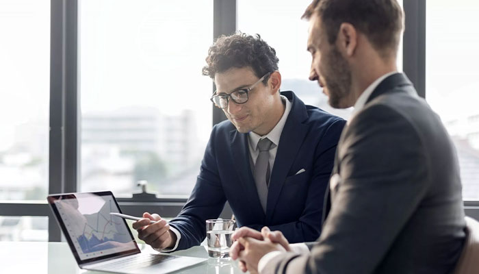 Mitarbeiterfluktuation beeinflusst den Unternehmenserfolg. Zwei Personalleiter bewerten die aktuellen Beschäftigtenzahlen an einem Laptop.