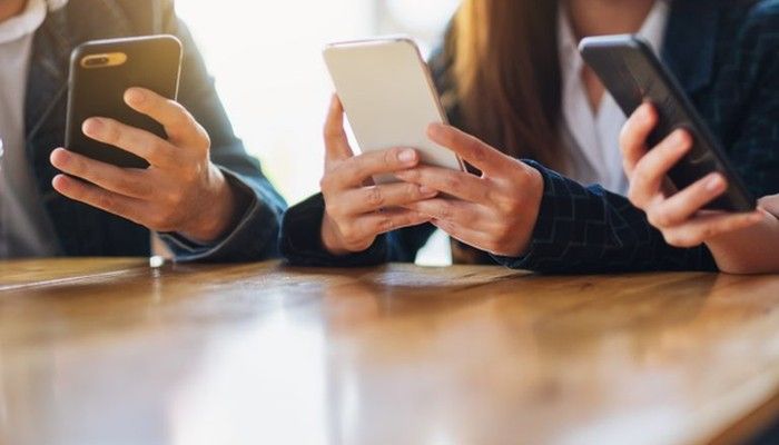 Eine Gruppe sitzt am Tisch und füllt am Smartphone gefälschte Fragebögen aus.
