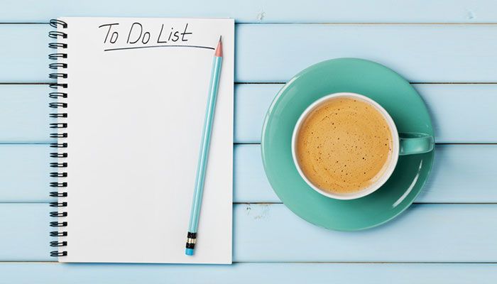 Auf einem Tisch steht ein Kaffee und ein Notizblock auf dem Checkliste Mitarbeiterbefragung steht.