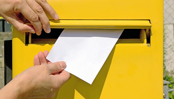 Einladung Online Befragung: Es wird einen Brief in einen gelben Briefkasten geworfen.