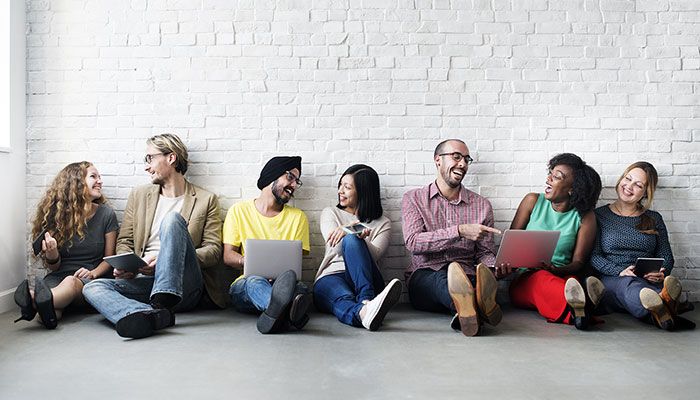 Menschen mit verschiedener Ethnografie sitzen nebeneinander auf dem Boden und füllen eine Befragung aus.