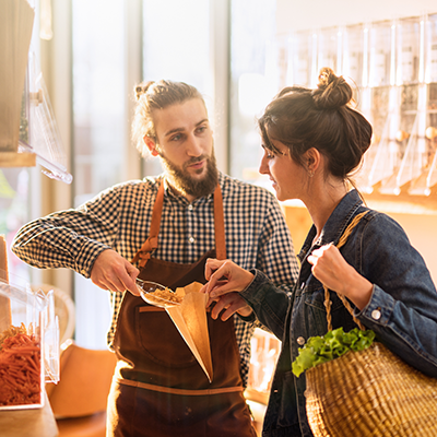 Ein Mitarbeiter hilft einer Kundin im Laden Nüsse in eine Tüte zu packen und stärkt dadurch die Kundenbindung.