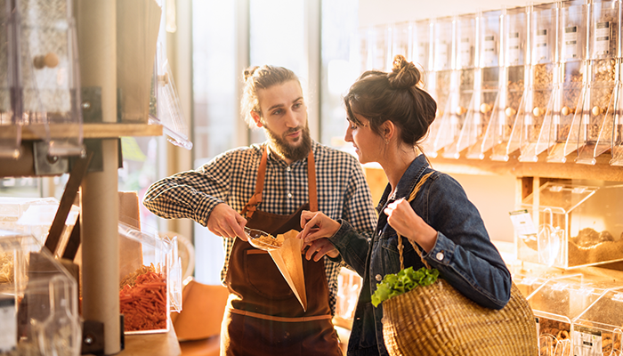 Ein Mitarbeiter hilft einer Kundin im Laden Nüsse in eine Tüte zu packen und stärkt dadurch die Kundenbindung.