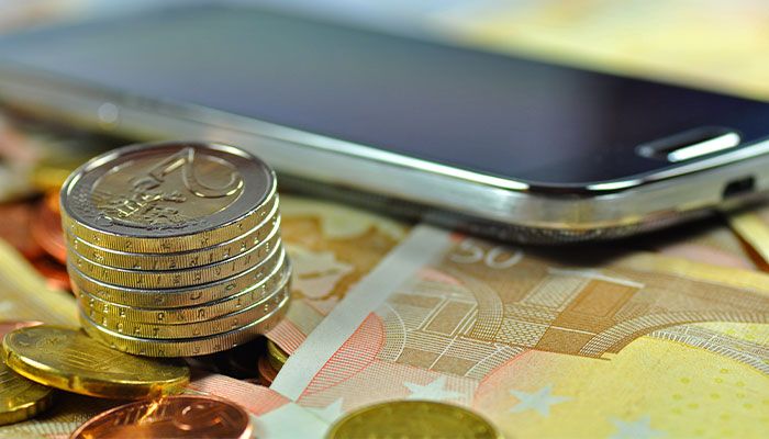 Smartphone liegt auf Geldscheinen und Münzenturm daneben