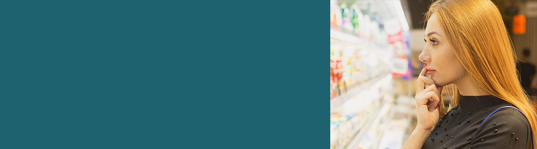 Eine junge Frau denkt über die Auswahl eines Joghurts im Kühlregal nach. Solche Situationen werden im Rahmen der Produktforschung beobachtet.