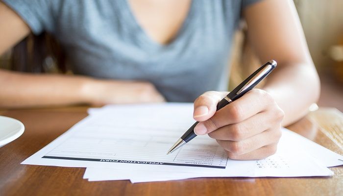 Close-up of woman filling application form in cafe. Unrecognizable young woman working with papers. She busy with documents. Paperwork concept
