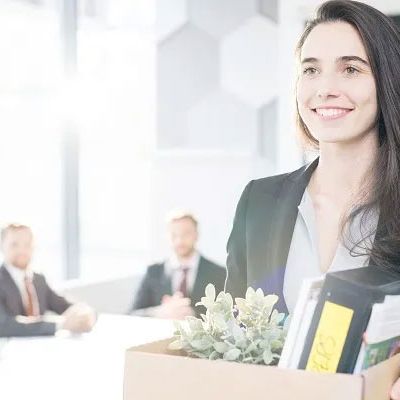 Junge Geschäftsfrau, die eine Kiste mit persönlichen Gegenständen in der Hand hält, als sie ihr Büro verlässt.
