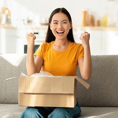 Umgang mit NPS-Feedback - junge Frau öffnet ein Paket und zeigt ihre Begeisterung über einen erfolgreichen Produktkauf indem sie lacht und ihre Hände in die Luft streckt.