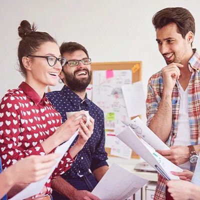 Team-Monitor: Fünf Personen stehen im Kreis mit Blättern in der Hand und lachen.