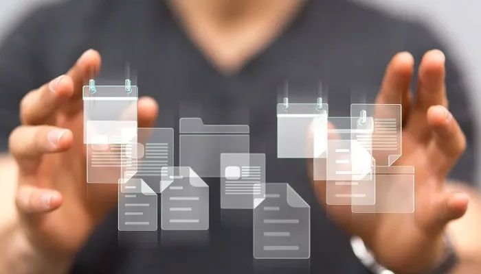 Zwei Hände halten viele Textdokumente die mit einer Textanalysesoftware bearbeitet werden müssen.