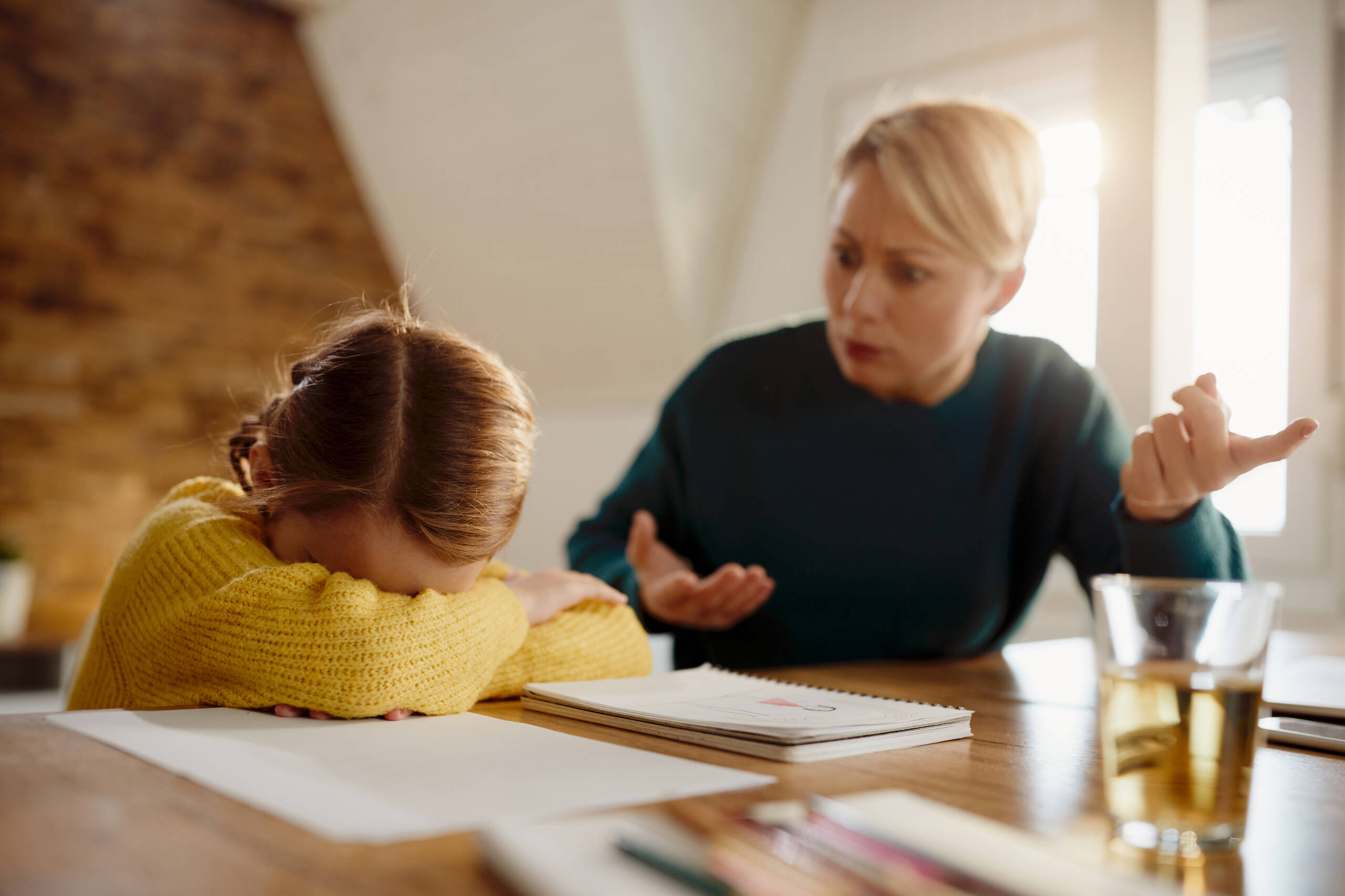 Little girl feeling sad while mother is scolding her during homeschooling.