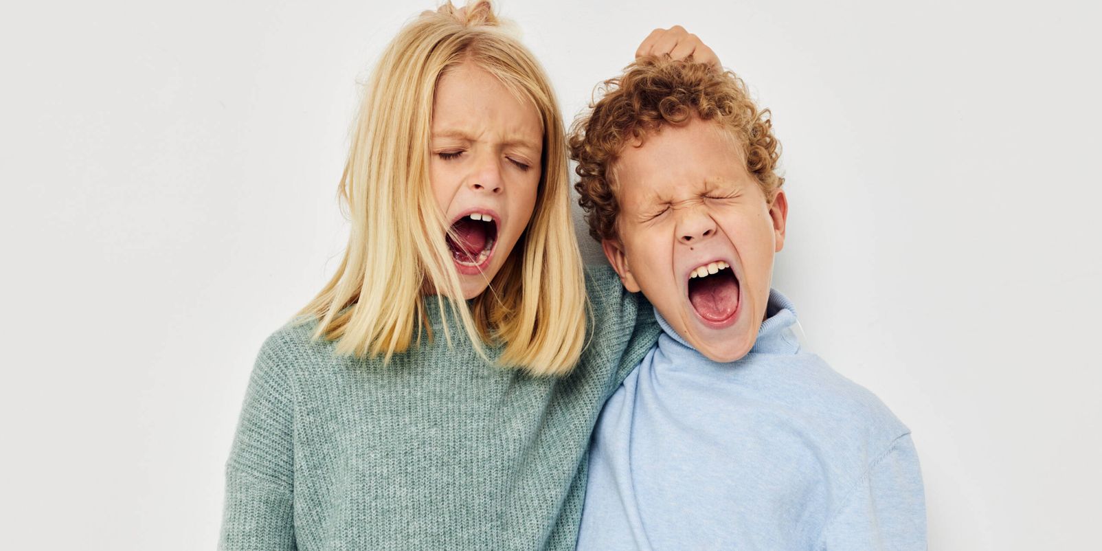 Photo of two children in multi-colored sweaters posing for fun light background. High quality photo