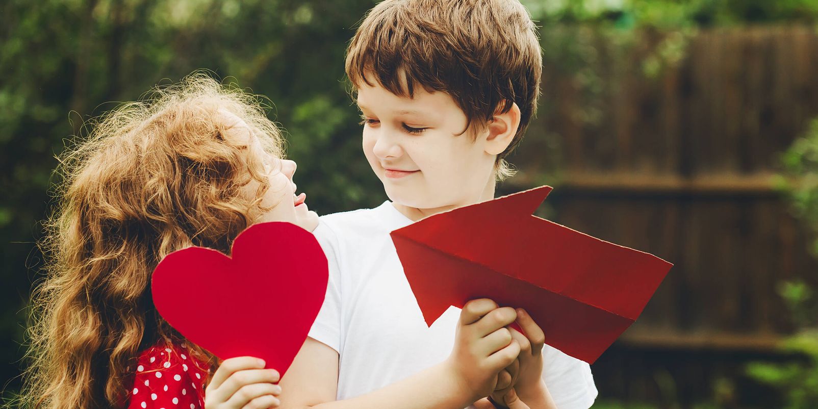 Cute children embrace and holding red heart shape in summer park. Valentines day background.