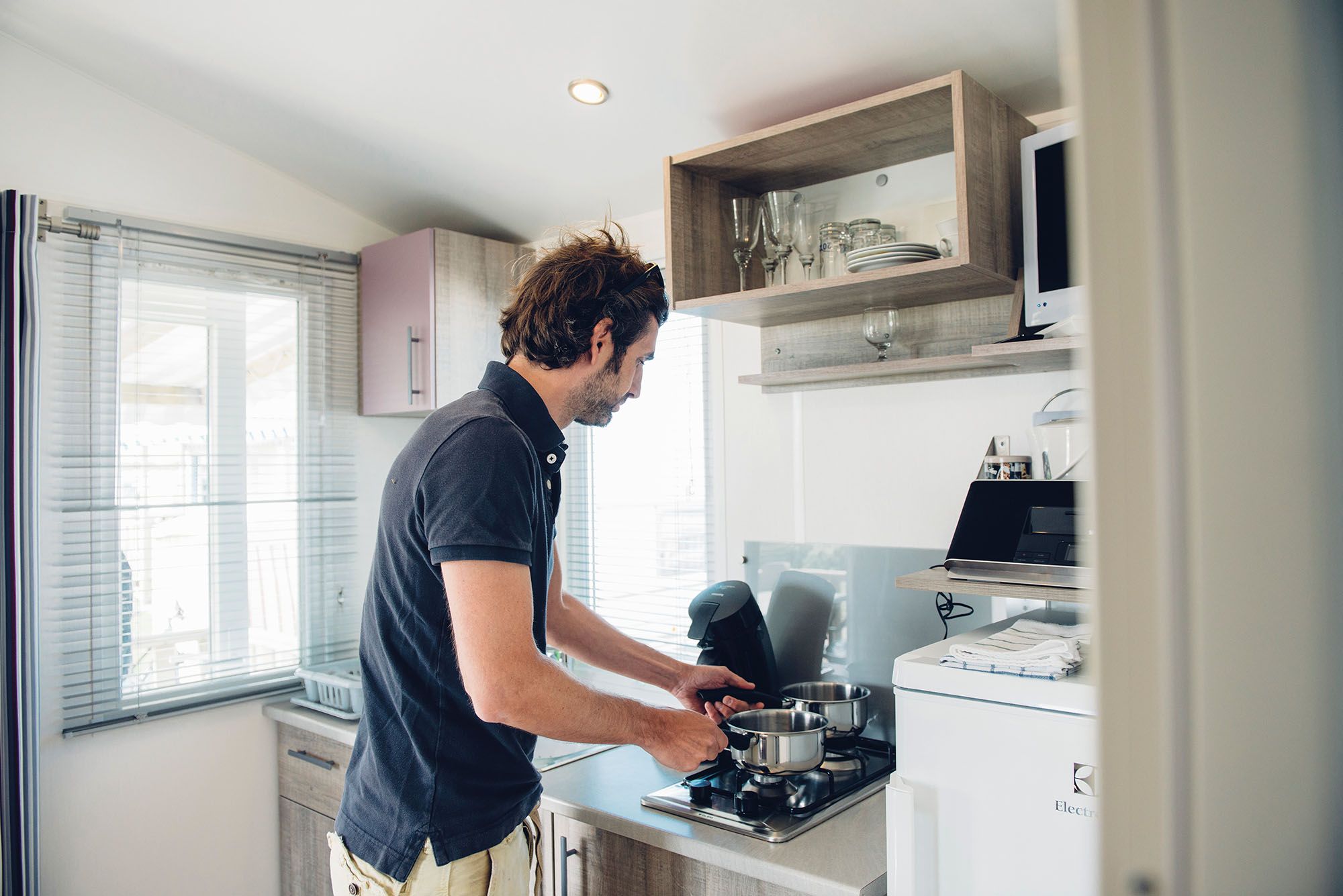 Mann bereitet in der Küche des kleinen Mobilheim auf dem Campingplatz Rantum eine kleine Mahlzeit zu