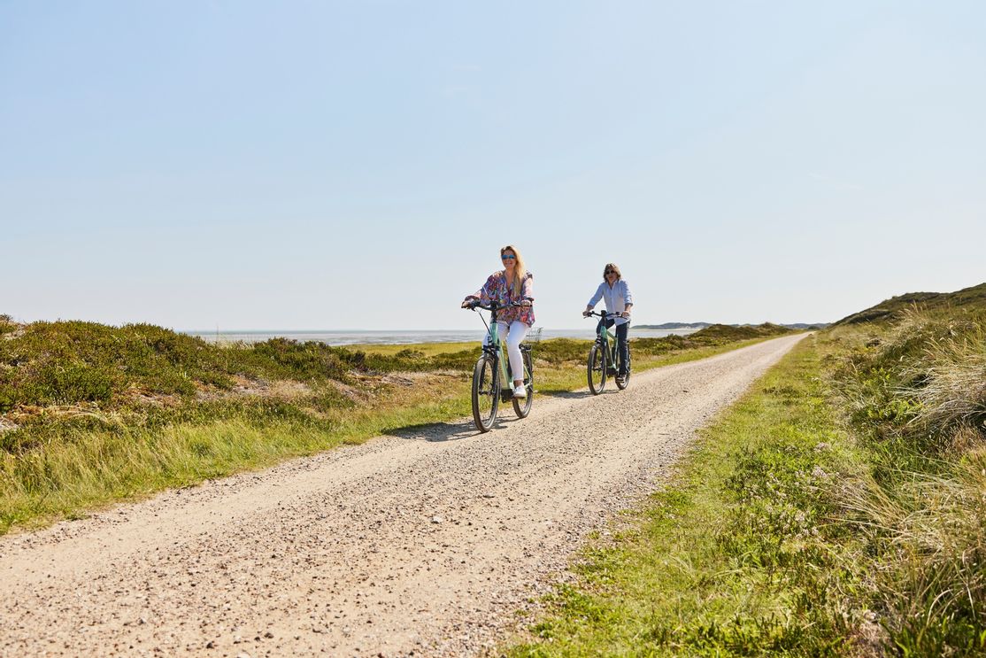Mann und Frau fahren mit E-Bikes auf dem geschotterten Fahrradweg in Rantum