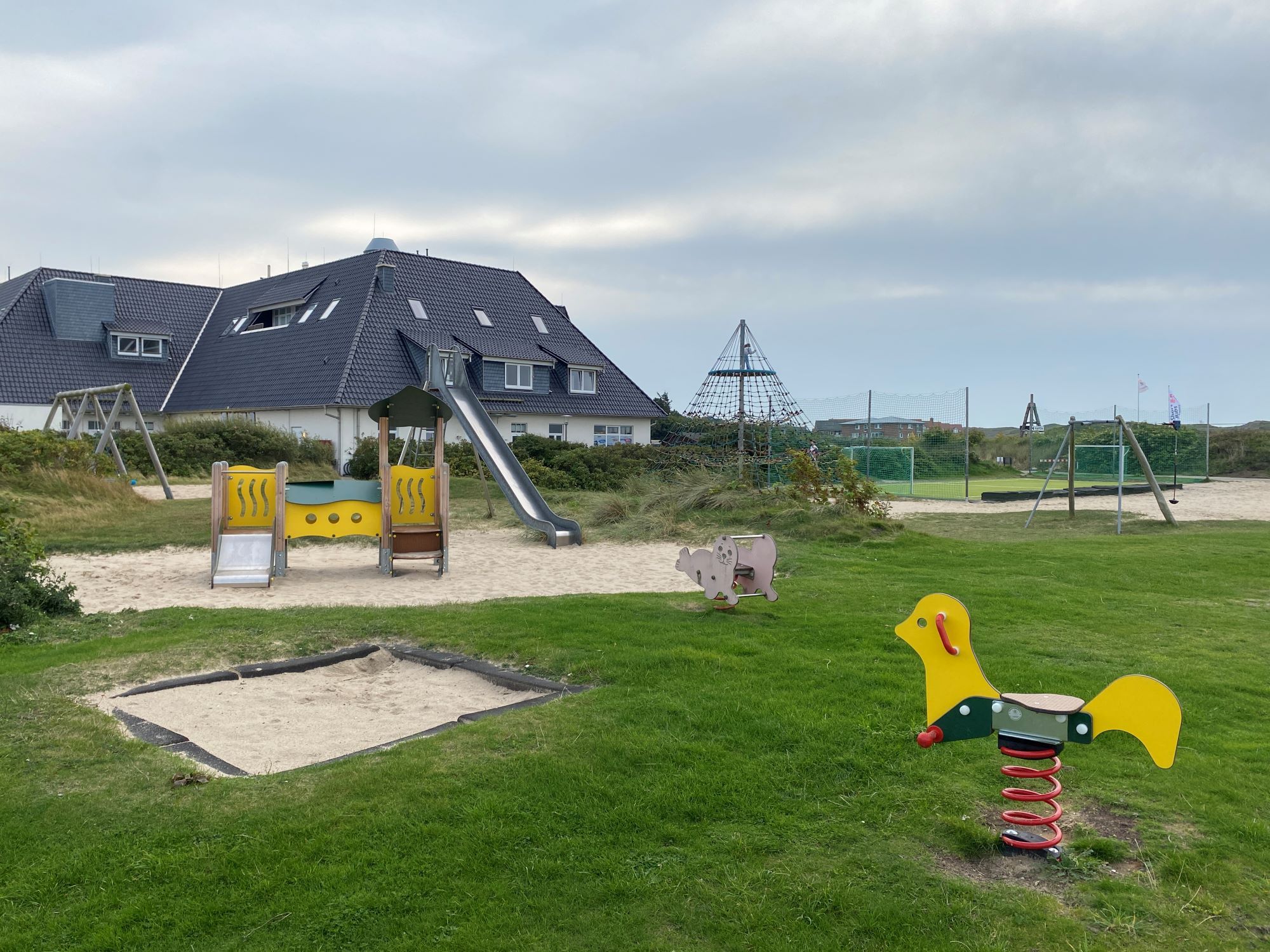 Spielplatz auf dem Campingplatz Rantum - im Vordergrund zwei Schaukeltiere, ein kleiner Sandkasten und das Kleinkinderspielgerät