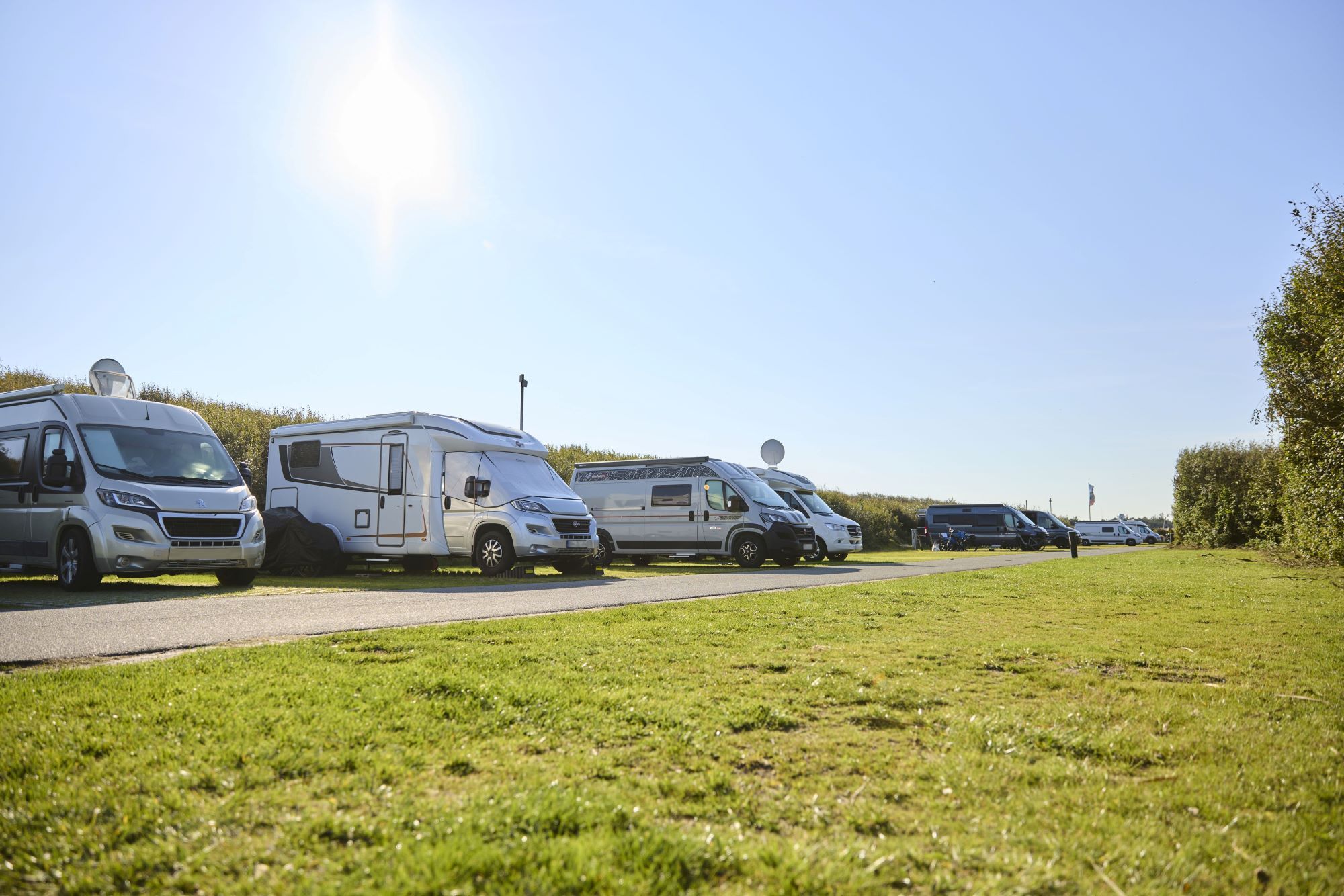 Wohnmobile auf den Wohnmobilplätzen auf dem Campingplatz Rantum, im Vordergrund grüne Wiese und ein befestigter Weg