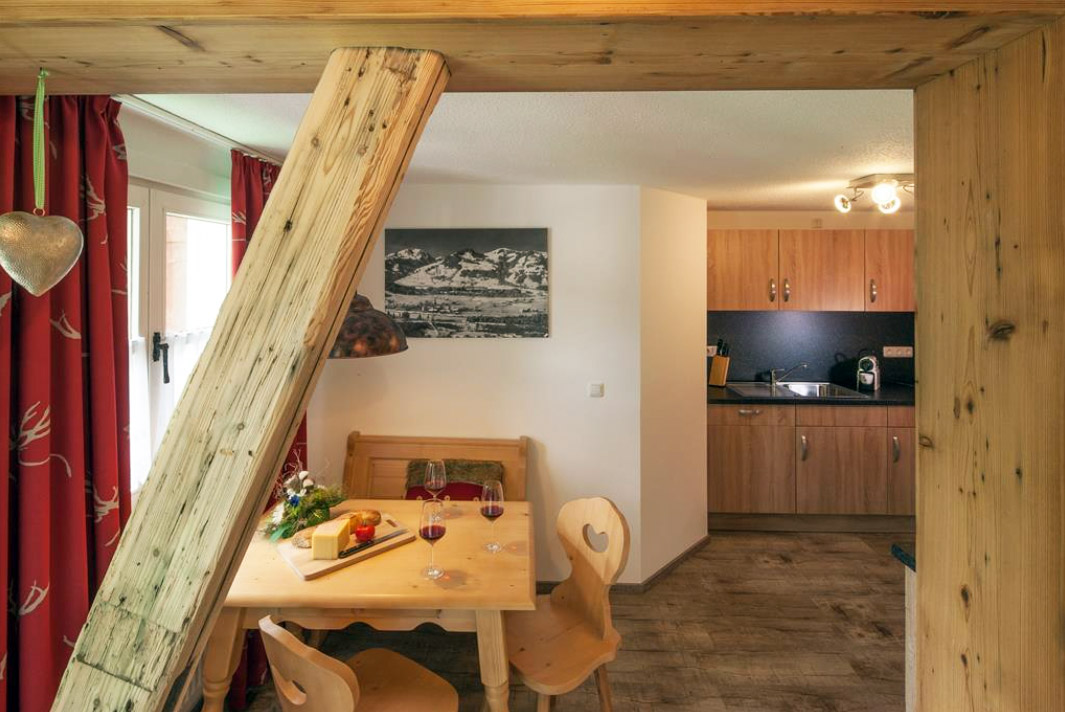 Gemütliches Wohnzimmer einer Ferienwohnung im Allgäu mit Holzoptik und voll ausgestatteter Küche – ideal für erholsame Urlaubstage in Fischen.