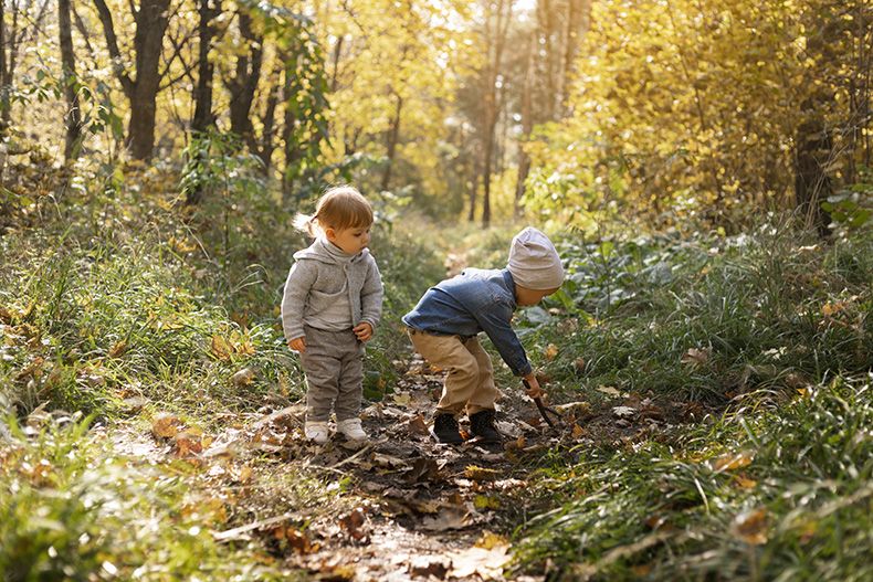Zwei Kinder in der Natur, eines hält einen Stock, beide schauen neugierig – spielerisches Entdecken im Allgäuer Freien.
