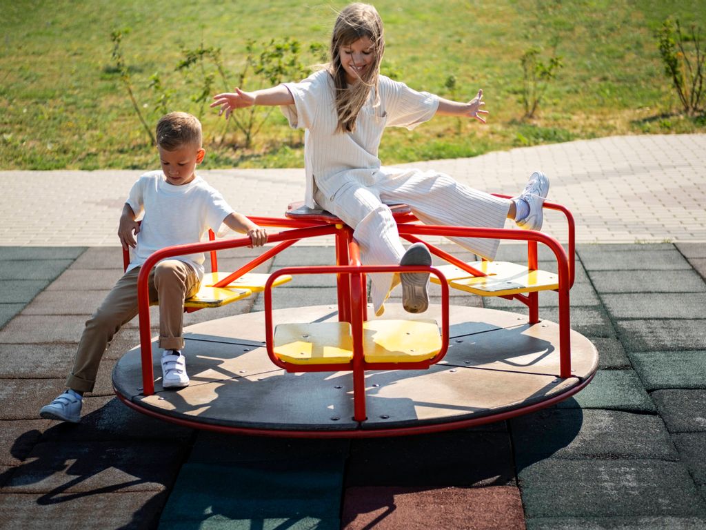 Bruder und Schwester haben Spaß auf einem drehbaren Spielgerät im Außenbereich – fröhliches Spielen auf dem Spielplatz im Allgäu.