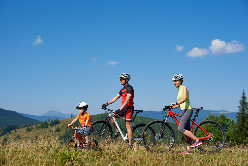 Eine Familie in sportlichen Outfits fährt mit einem kleinen Kind durch eine Berglandschaft.