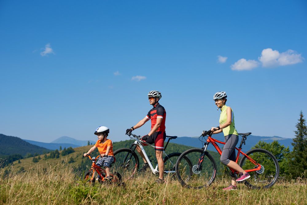 Eine Familie in sportlichen Outfits fährt mit einem kleinen Kind durch eine Berglandschaft.