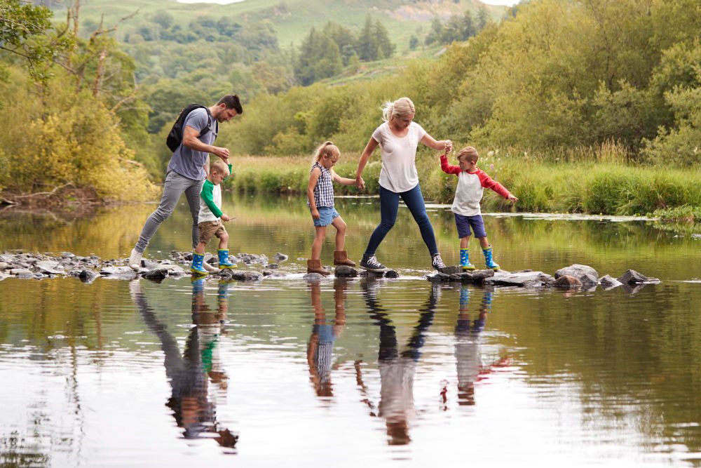 Eine Familie mit drei kleinen Kindern wandert und überkehrt auf Steinen einen Fluss.