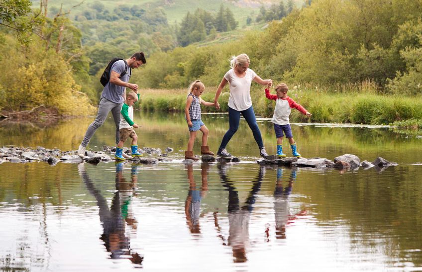 Eine Familie mit drei kleinen Kindern wandert und überkehrt auf Steinen einen Fluss.